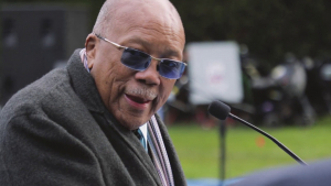 An older man wearing glasses speaks into the mic.