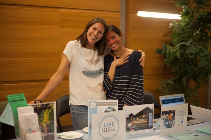Two women smile and hug in front of a table for Semel HCI.