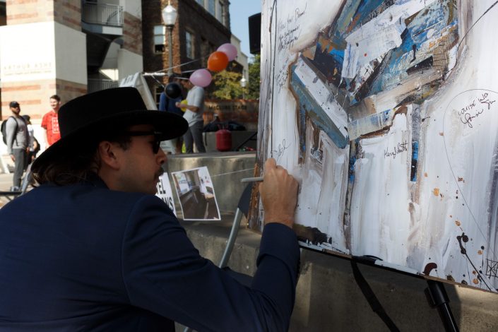 Man signs a painting of a piano.