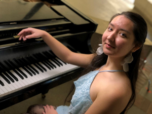 A woman sits next to a grand piano.