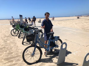 A woman smiles, holding a thumbs up next to her bicycle.