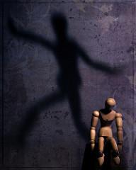 A mannequin doll is hunched over, while its shadow dances.