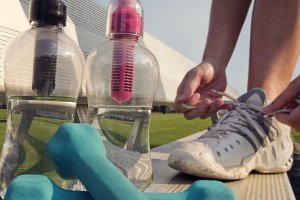 An individual ties their shoes next to water bottles and dumbbells.