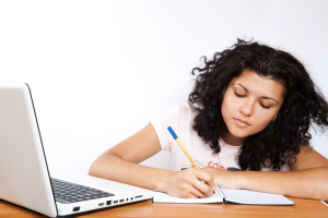 A student studies on a notebook next to her laptop.