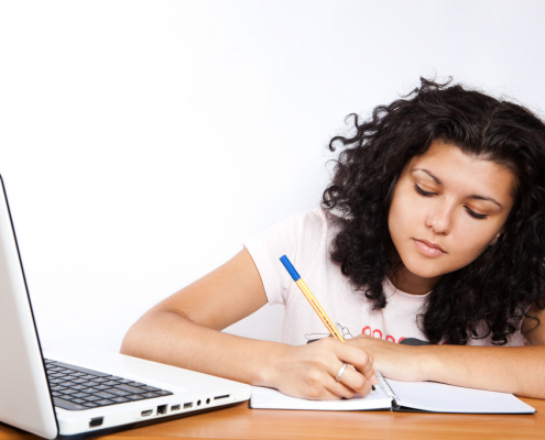 A student studies on a notebook next to her laptop.