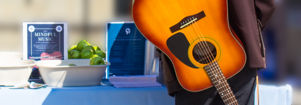 A man fills out a form with his guitar strapped to his back.