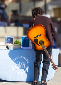A man fills out a form with his guitar strapped to his back.