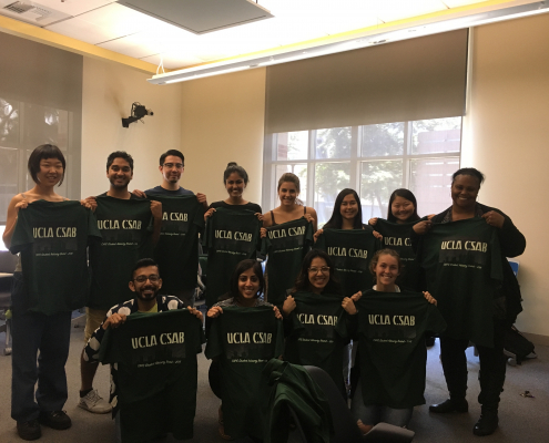 A group of individuals hold up UCLA CSAB t-shirts.