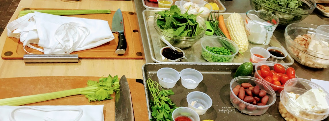 Photo of a kitchen with a cutting board, an apron, celery and a knife as well as various other ingredients.