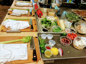 Photo of a kitchen with a cutting board, an apron, celery and a knife as well as various other ingredients.