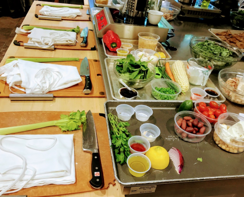 Photo of a kitchen with a cutting board, an apron, celery and a knife as well as various other ingredients.