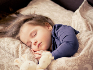 A young child sleeps comfortably in their bed with a stuffed animal.