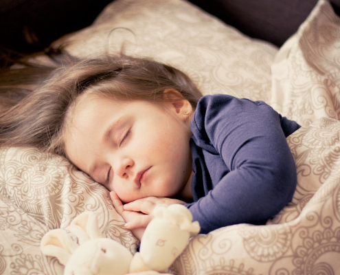 A young child sleeps comfortably in their bed with a stuffed animal.