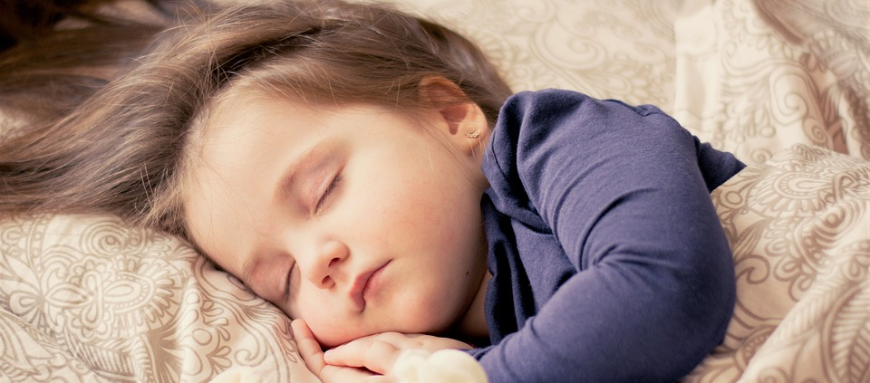 A young child sleeps comfortably in their bed with a stuffed animal.