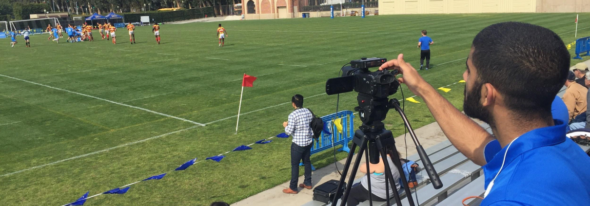 A person films a field of people playing soccer.