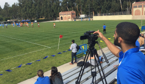 A person films a field of people playing soccer.