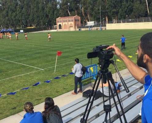 A person films a field of people playing soccer.