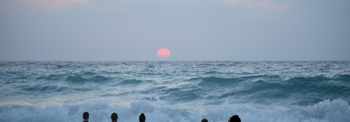 A group of people sitting on the sand looking out at the ocean.