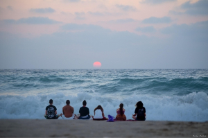 A group of people sitting on the sand looking out at the ocean.