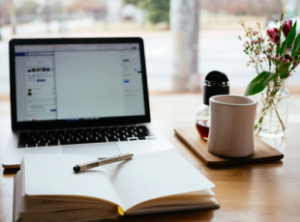 A photo of an open journal in front of a computer and mug.