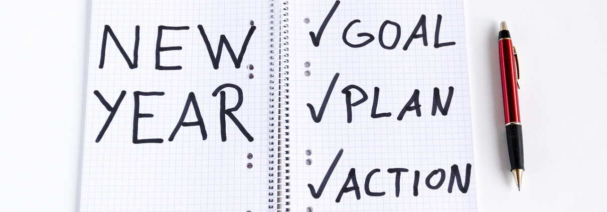 A notebook has New Year, and checked off goal, plan and action written in it.