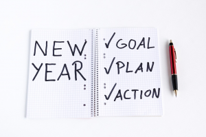 A notebook has New Year, and checked off goal, plan and action written in it.