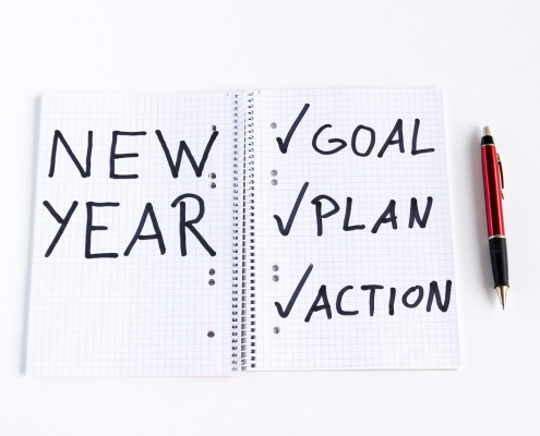 A notebook has New Year, and checked off goal, plan and action written in it.