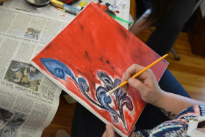 An individual paints blue swirls on a red canvas.