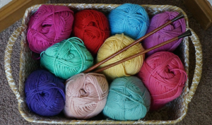 A container of brightly colored yarn with knitting needles placed in the middle.