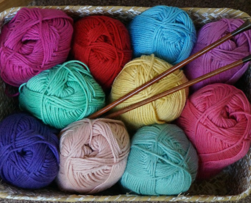 A container of brightly colored yarn with knitting needles placed in the middle.