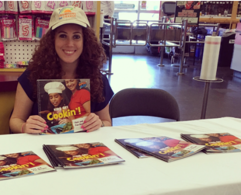 A woman holding a 'Kids get Cookin'!' book.