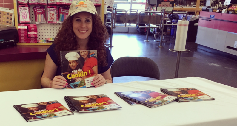 A woman holding a 'Kids get Cookin'!' book.