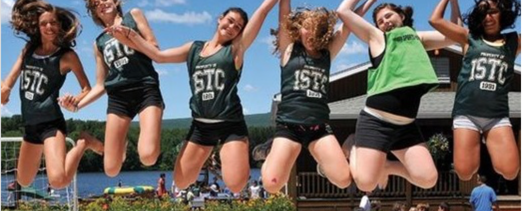A group of students jump while raising and holding their hands with one another.