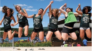 A group of students jump while raising and holding their hands with one another.