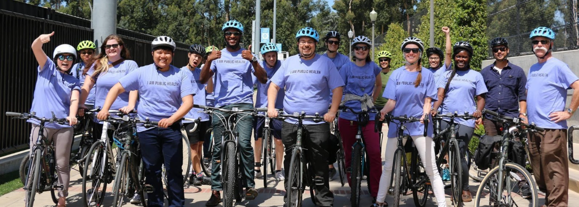 A group of individuals stand next to their bikes with helmets on, wearing Law Public Health t-shirts.