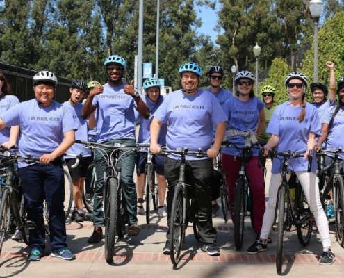 A group of individuals stand next to their bikes with helmets on, wearing Law Public Health t-shirts.