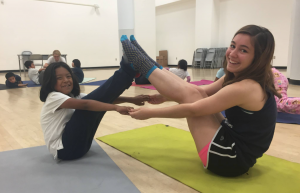2 students hold a yoga pose with one another.