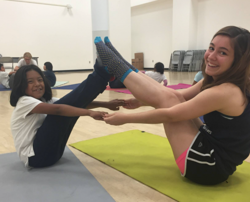 2 students hold a yoga pose with one another.