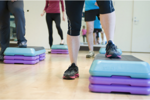 A person elevates their foot on a small stand in a fitness class.