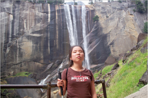 A girl poses in front of a waterfall holding a white cane.