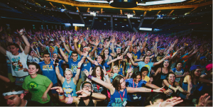 A very large crowd of students hold both of their arms up and out.