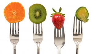 Four forks slice skewered through orange, kiwi, strawberry and Brussel sprout.