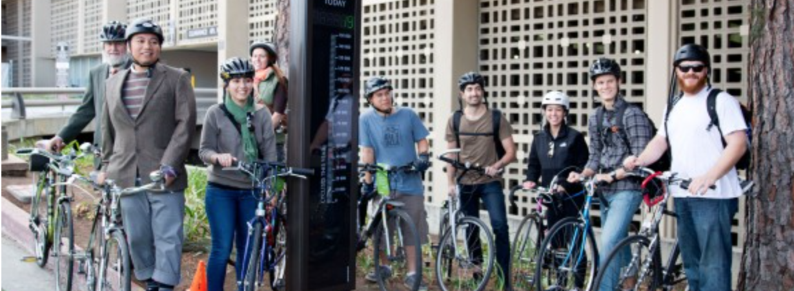 A group of individuals stand next to their bikes with helmets on.