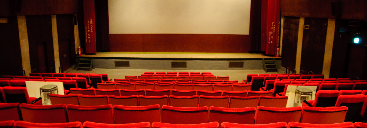 A lit-up empty theater filled with brilliant red seats and gold accents.