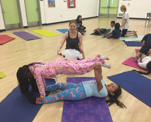 Multiple children strike fun yoga poses with one another.