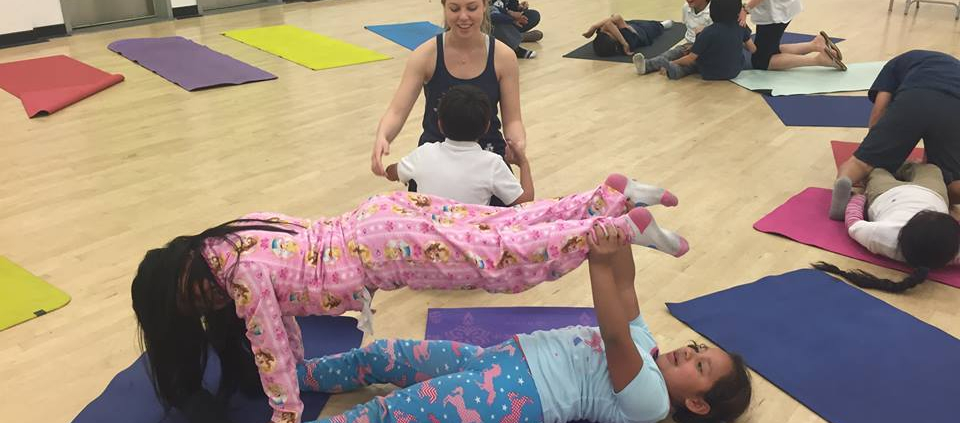 Multiple children strike fun yoga poses with one another.